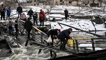 مدنيون يعبرون جسرا مدمّرا على الجبهة الشمالية في كييف (1 آذار 2022، أ ف ب). 
