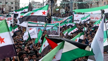 سوريون يرفعون الأعلام خلال مسيرة في إدلب في الذكرى الـ11 على بدء الانتفاضة ضد النظام السوري (15 آذار 2022ـ أ ف ب). 