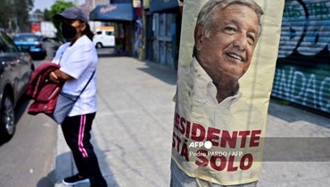 امرأة تقف بجانب ملصق يروج للاستشارة الشعبية حول إلغاء تفويض الرئيس المكسيكي أندريس مانويل لوبيز أوبرادور في إكستابالوكا، ولاية المكسيك (أ ف ب).