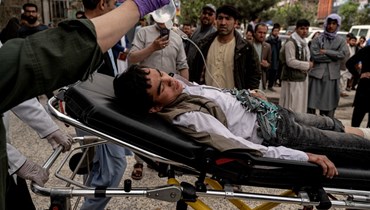 عاملون طبيون ينقلون شابًا جريحاً خارج مستشفى في كابول، بعد انفجار قنبلتين في مدرسة للبنين في حي الهزارة الشيعي (19 نيسان 2022، أ ف ب). 