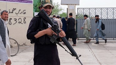 مقاتل من طالبان يقف قرب مستشفى في كابول، بينما وصل أقارب ضحايا (في الخلفية) للبحث عن أحبائهم بعد انفجار قنبلتين في مدرسة للبنين في حي الهزارة الشيعي (19 نيسان 2022، أ ف ب). 