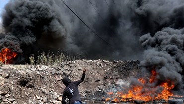 فلسطيني يرشق قوات الأمن الإسرائيلية بالحجارة خلال اشتباكات في أعقاب تظاهرة ضد مصادرة إسرائيل للأراضي، في قرية كفر قدوم بالقرب من مستوطنة كدوميم اليهودية في الضفة الغربية المحتلة (6 ايار 2022، ا ف ب). 