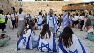 متظاهرات تدثرن بالأعلام الإسرائيلية وجلسن بالقرب من حائط المبكى في البلدة القديمة بالقدس خلال "مسيرة الأعلام" الإسرائيلية (29 ايار 2022، أ ف ب). 