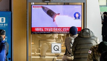 اشخاص جلسوا قرب شاشة تلفزيون في محطة قطارات بسيول، تعرض بثًا إخباريًا مع لقطات لتجربة صاروخ كوري شمالي (18 ت2 2022، أ ف ب). 