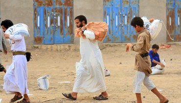 رجال يمنيون يحملون مساعدات إنسانية تم توزيعها على نازحين في ضواحي مدينة مأرب شمال شرق اليمن (6 نيسان 2023، أ ف ب). 