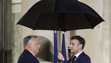 ماكرون (الى اليمين) يحمل مظلة خلال ترحيبه بأوربان في قصر الإليزيه في باريس (7 ك1 2023، أ ف ب). 