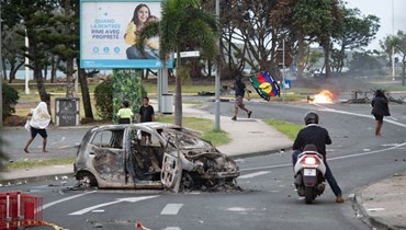 أشخاص يمرون قرب سيارة محترقة من جراء اعمال عنف في منطقة نجيا في نوميا (14 ايار 2024، أ ف ب). 