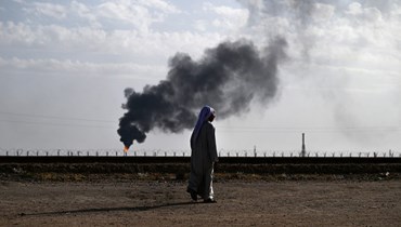 أحد السكان المحليين حسين جلود يسير أمام منزله بينما يتصاعد الدخان من احتراق الغاز في حقل الرميلة النفطي القريب في محافظة البصرة جنوب العراق، في (5 أيار 2024- أ ف ب).