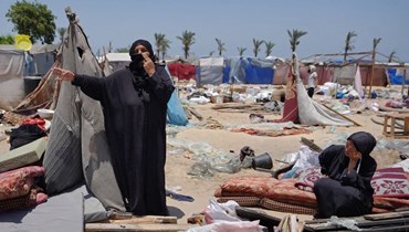 نساء فلسطينيات نازحات وقفن بجانب ممتلكاتهن بينما يخلي فلسطينيون منطقة المواصي على مشارف جنوب غرب خان يونس في جنوب قطاع غزة (28 حزيران 2024، أ ف ب). 