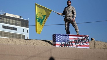  رجل يحمل علم "حزب الله" يقف على علم أميركا.