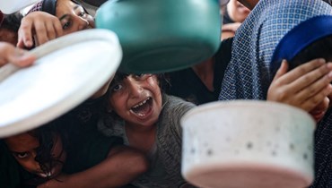 نساء وأطفال فلسطينيّون يحاولون الحصول على حصتهم من الطعام الذي أعدّه متطوعون في بيت لاهيا، شمال قطاع غزة (أ ف ب). 